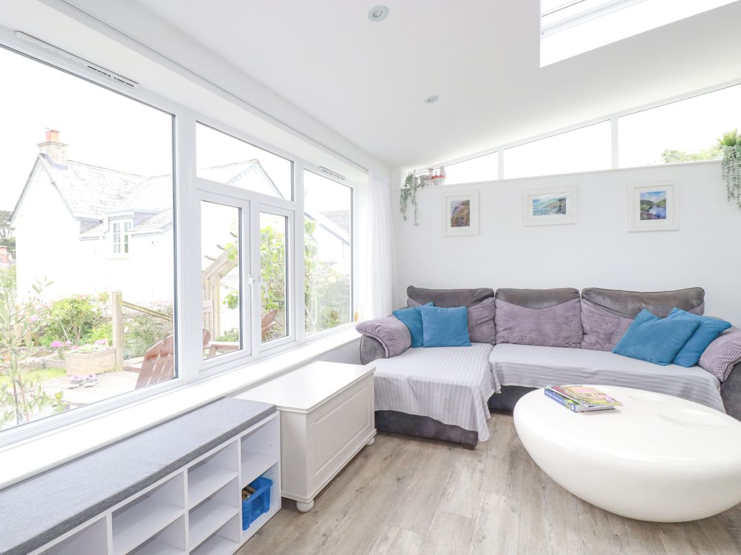 A sitting area with a large sectional sofa blue pillows white storage bench and an oval white coffee table at Langurra in Crantock
