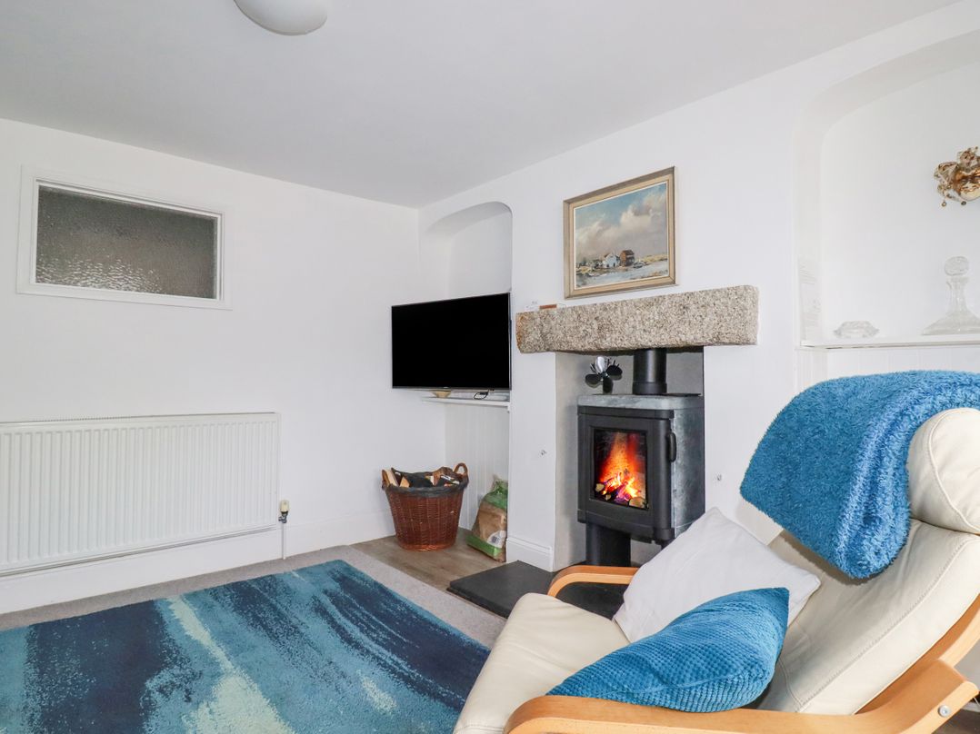 A living room with a fireplace a television a wicker basket with firewood and a chair with blue cushions and blanket at Langurra in Crantock