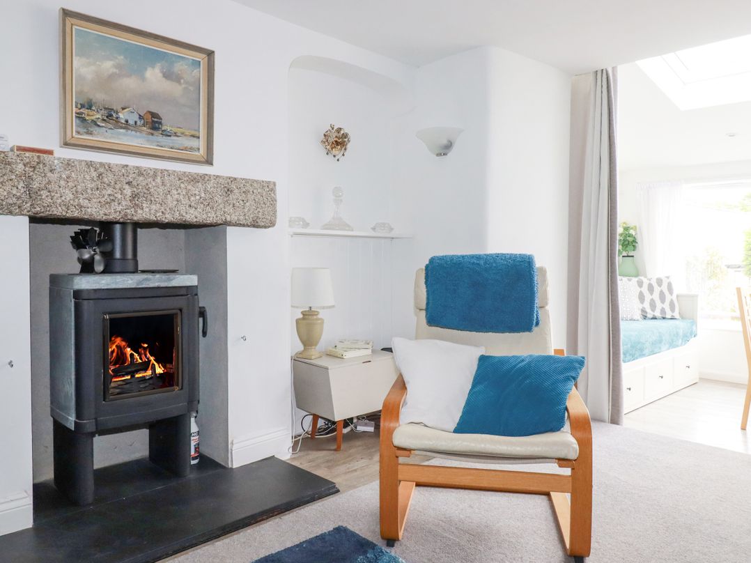 A living room with a wood stove fireplace a chair with blue and white cushions and a small side table with a lamp at Langurra in Crantock