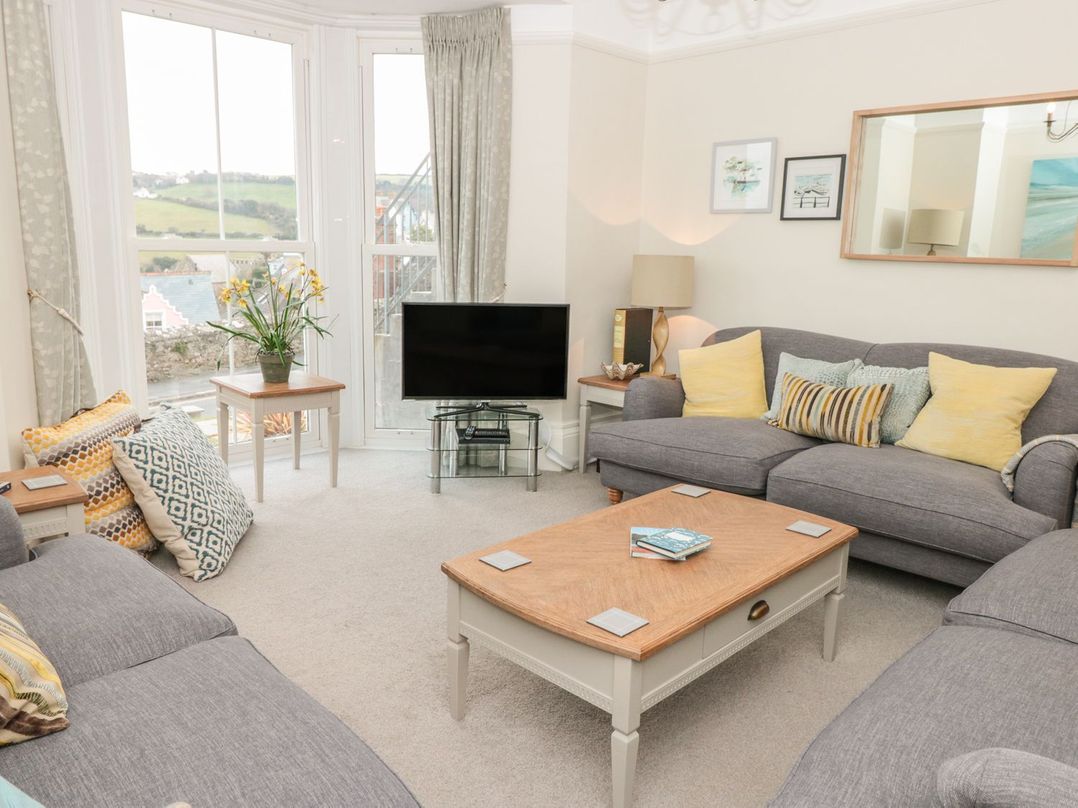 A living room with gray sofas yellow and patterned cushions a wooden coffee table a flat screen tv near large windows at Leylands in Salcombe