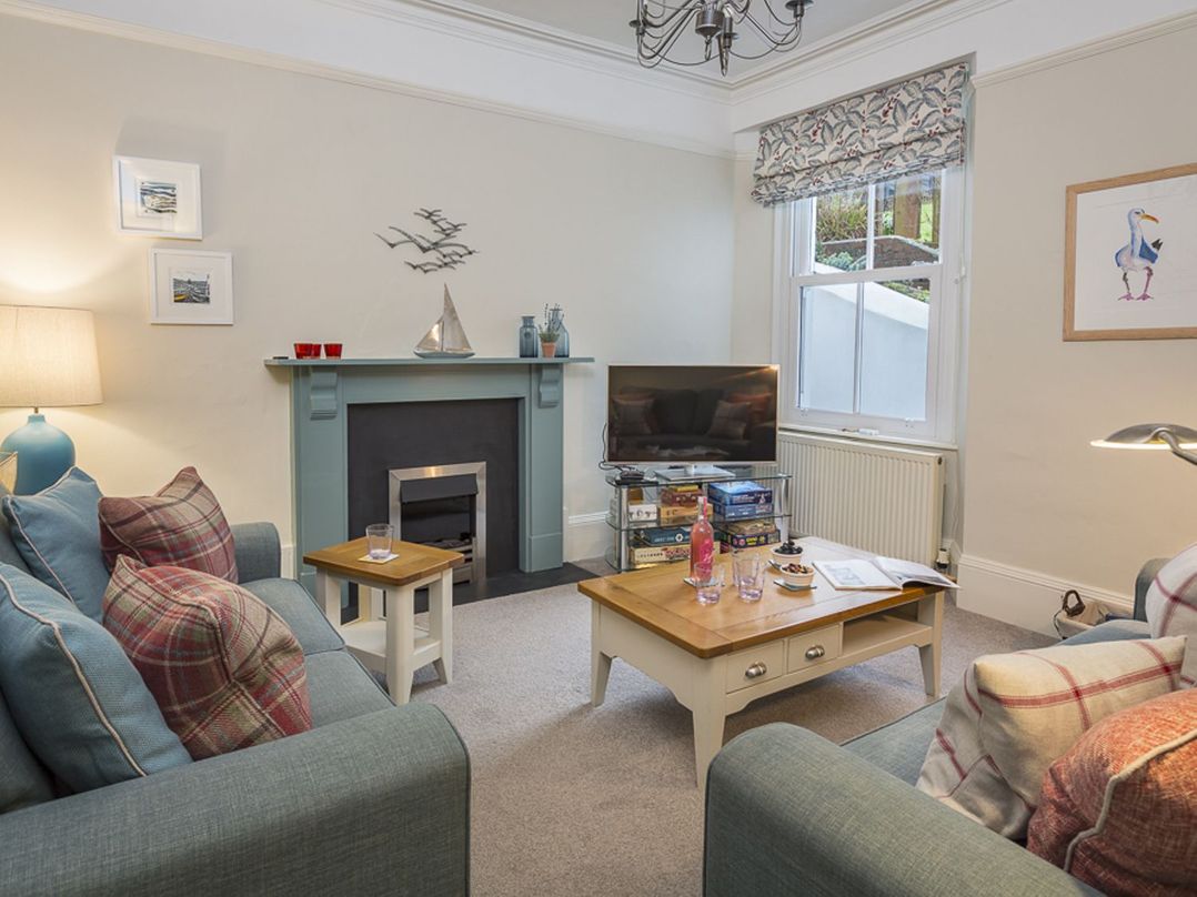 A living room with blue sofas, coffee table, fireplace, TV, and window at Leylands in Salcombe