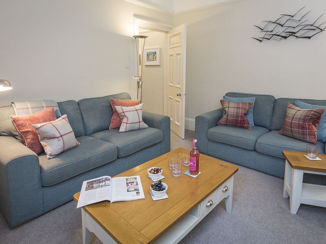 A living room with two blue sofas and a wooden coffee table with snacks and a pink drink at Leylands in Salcombe