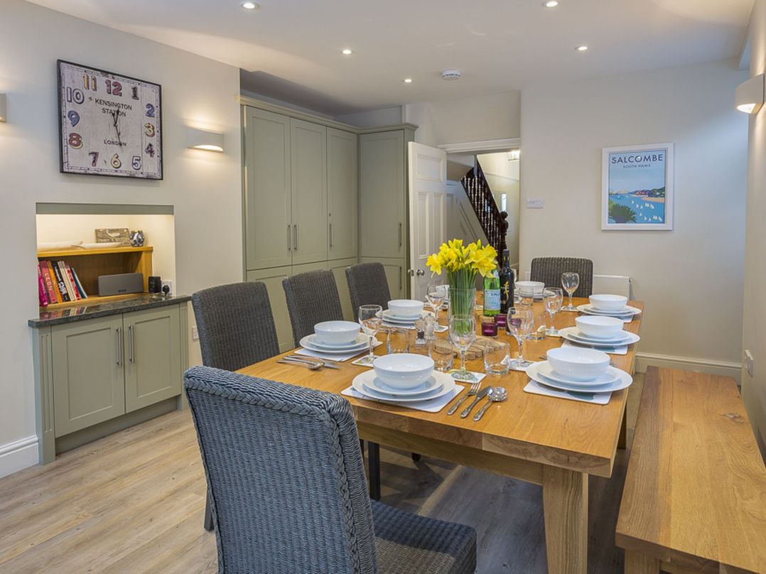A dining room with a wooden table set for eight with plates glasses and cutlery with grey chairs and a wooden bench at Leylands in Salcombe