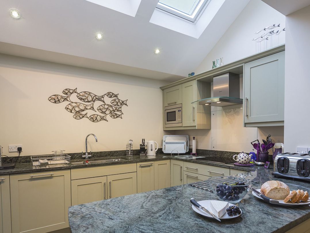 A kitchen with green cabinets and granite countertops with a bowl of grapes and sliced bread on the counter at Leylands Salcombe