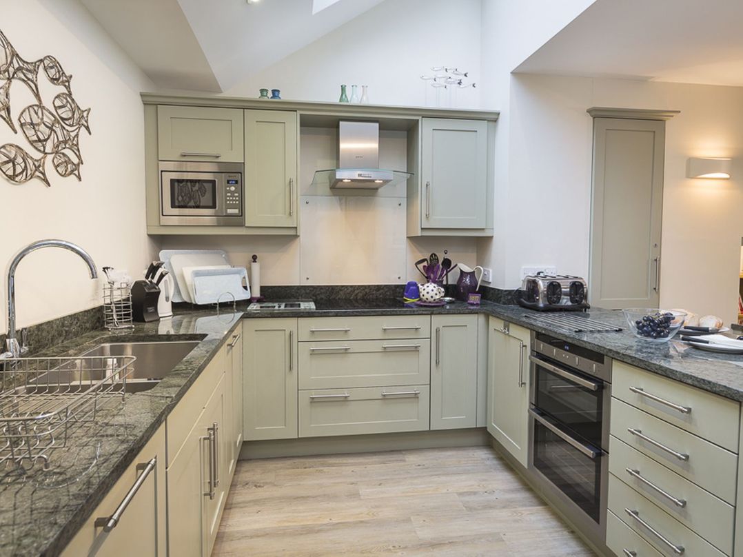 A kitchen with light green cabinets black granite countertops built-in microwave oven and toaster at Leylands Salcombe