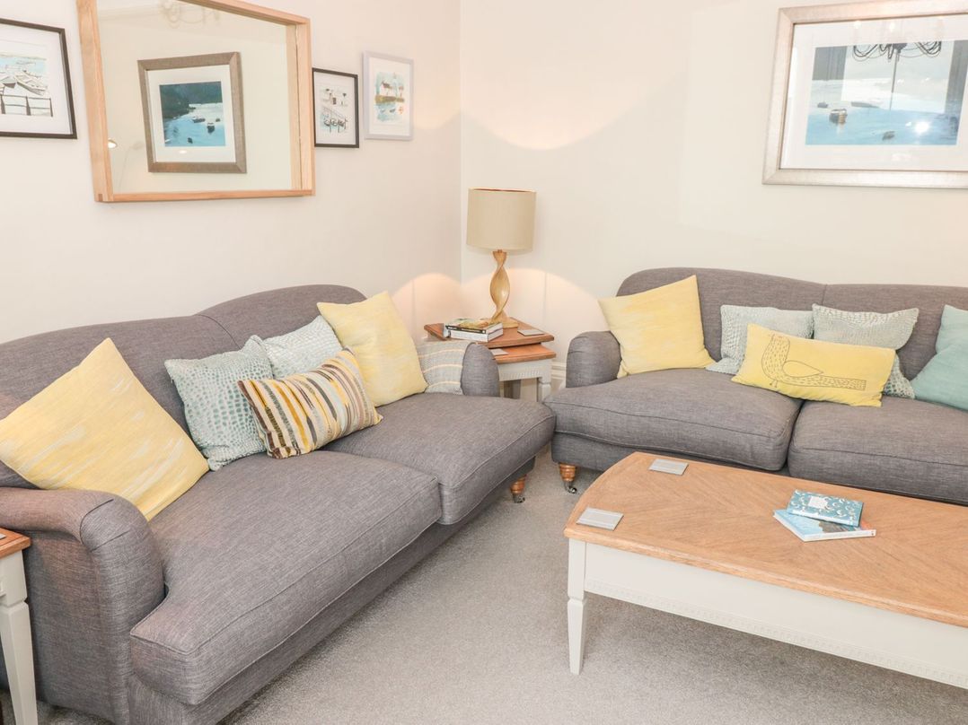 A living room with two gray sofas yellow and patterned cushions a wooden coffee table and framed pictures on the walls at Leylands in Salcombe