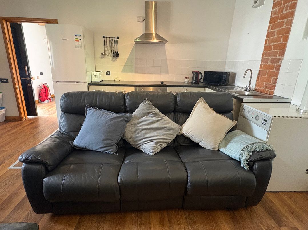 A living room with a sofa in front of a kitchen at Woodside Cottage in Kerry