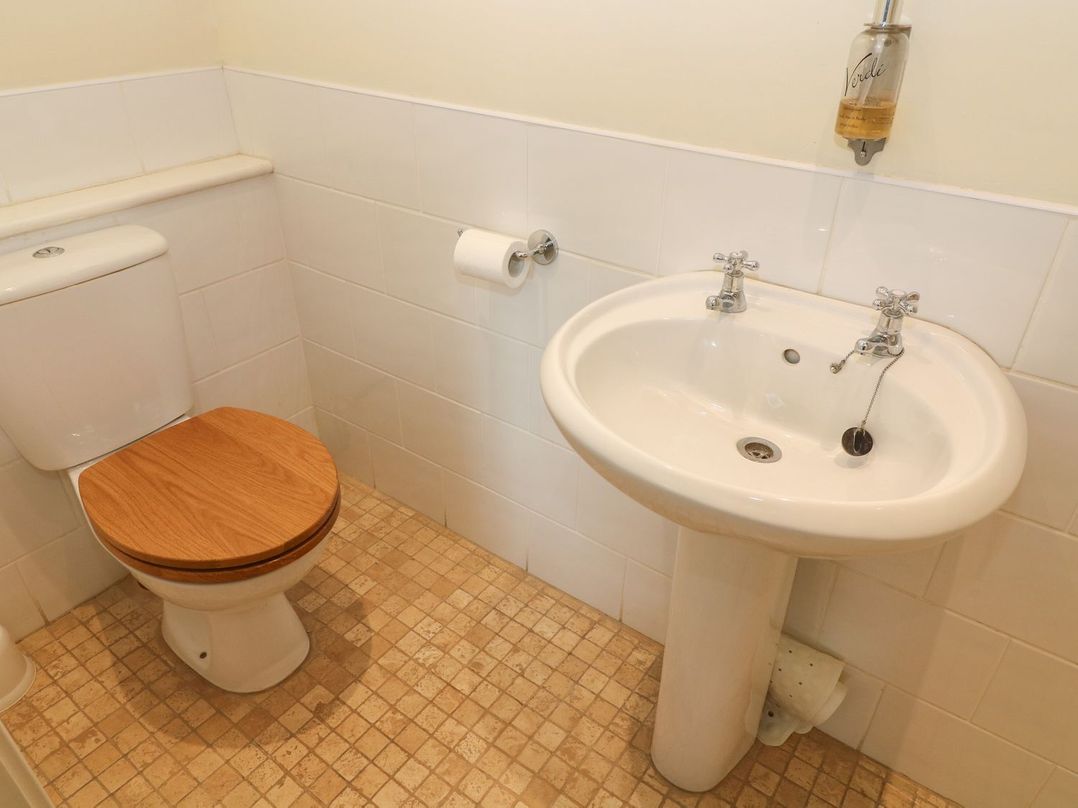 A bathroom with a toilet with a wooden seat a pedestal sink and a soap dispenser at Kearton Shunner Fell Thwaite near Muker