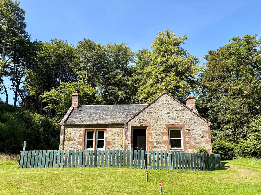 A house with a fence and trees in the vicinity at Gunroom Cottage in Castle Leod near Strathpeffer