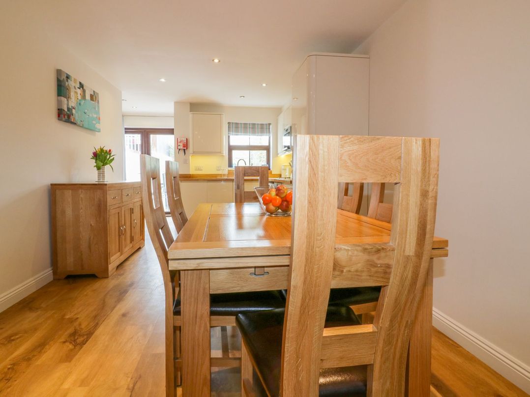 A dining area with a wooden table and chairs a bowl of fruit on the table and a sideboard with flowers at The Beach Hut in Crantock near Newquay
