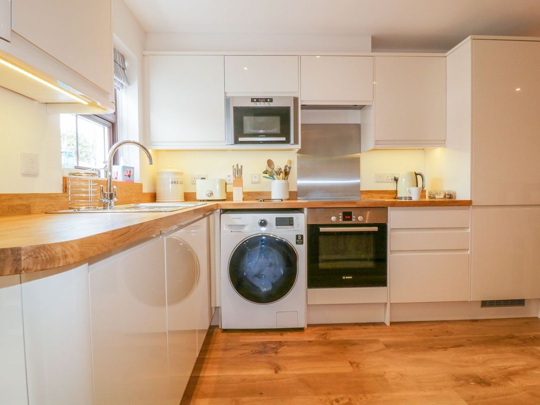 A modern kitchen with wooden countertops a washing machine an oven microwave kettle and utensils at The Beach Hut in Crantock near Newquay