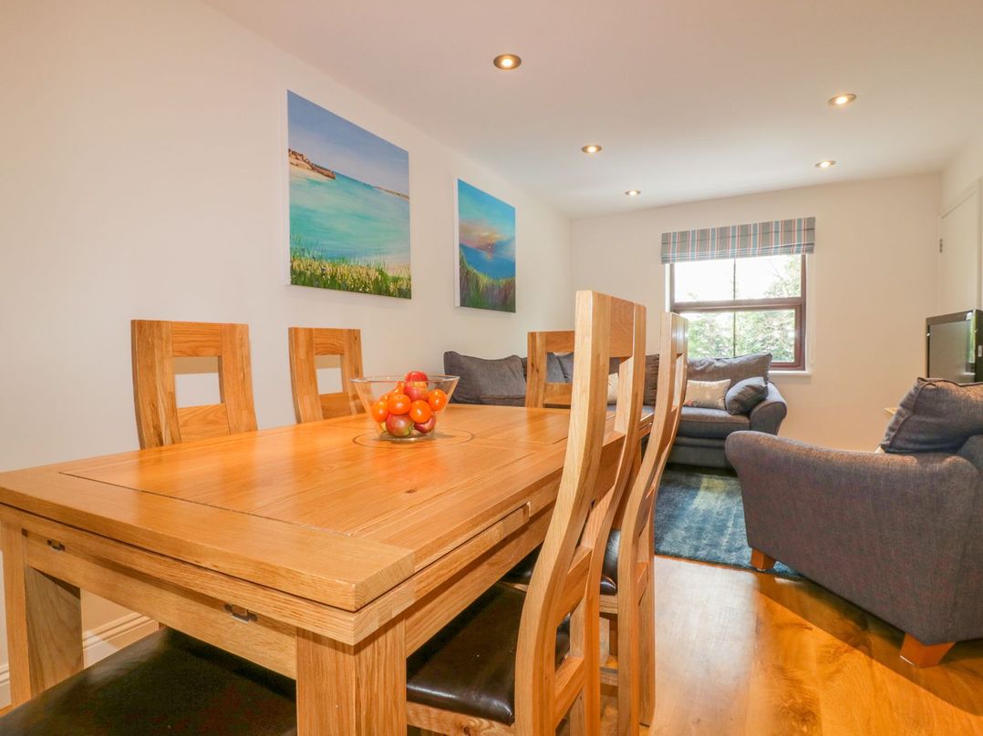 A dining area with a wooden table and chairs next to a living space with sofas and a window at The Beach Hut in Crantock near Newquay