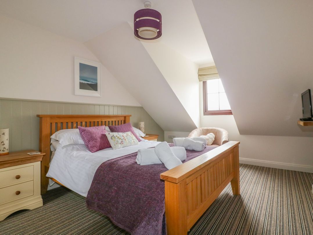 A bedroom with a wooden bed with purple pillows and blanket a striped carpet a window and a chair at The Beach Hut in Crantock near Newquay