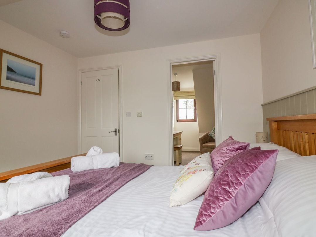 A bedroom with a wooden bed with purple and white pillows and rolled towels on the bed at The Beach Hut in Crantock near Newquay
