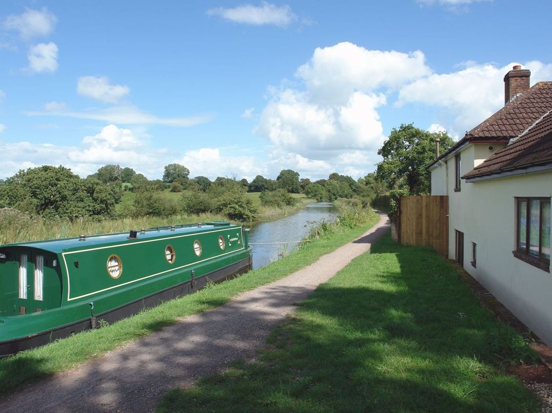 A canal boat moored next to a path by a river with a house on the right at Valley House in Halberton near Tiverton