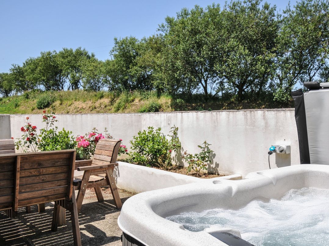 An outdoor area with a hot tub and wooden dining furniture at The Dairy Barn in Camelford