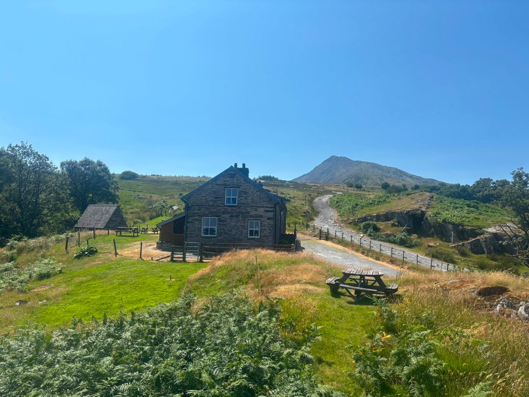 A house with a mountain in the background and a picnic table at Ty Siabod in Capel Curig near Betws-Y-Coed
