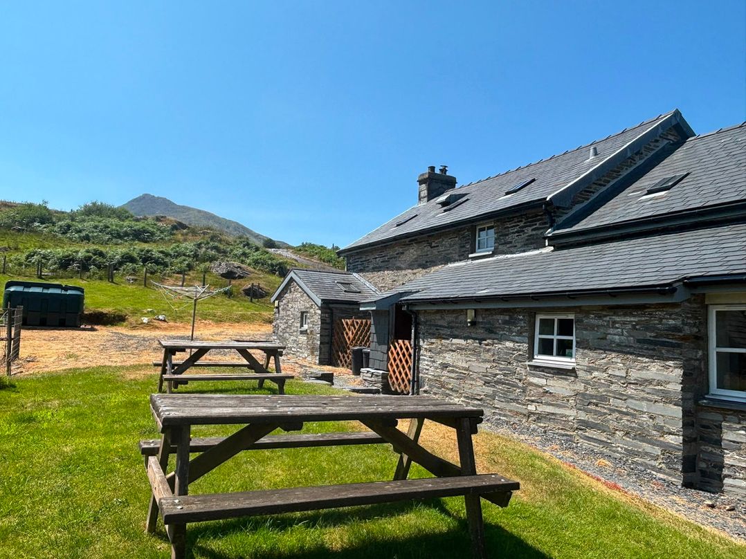 An outdoor area with benches and a cottage at Ty Siabod in Capel Curig near Betws-Y-Coed