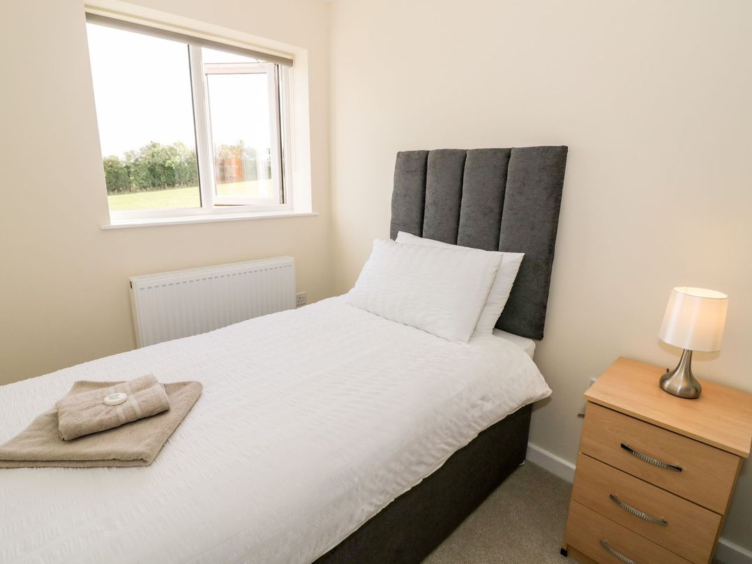 A bedroom with a single bed with white bedding a bedside table with a lamp and a window with a view of greenery at Walnut Cottage in Welford-On-Avon