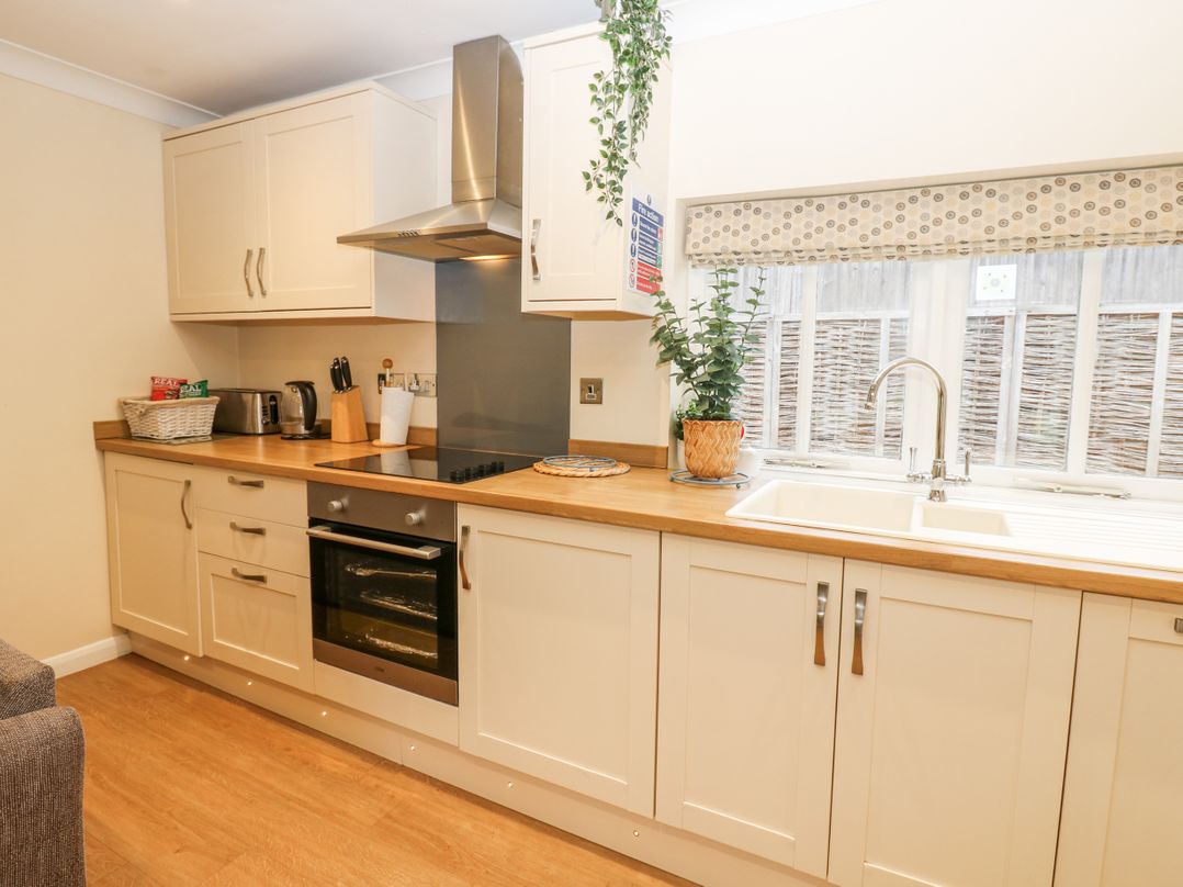 A kitchen with white cabinets wooden countertop an oven a stovetop a stainless steel hood a sink and a window at Walworth Castle Holiday Cottage Walworth near Darlington
