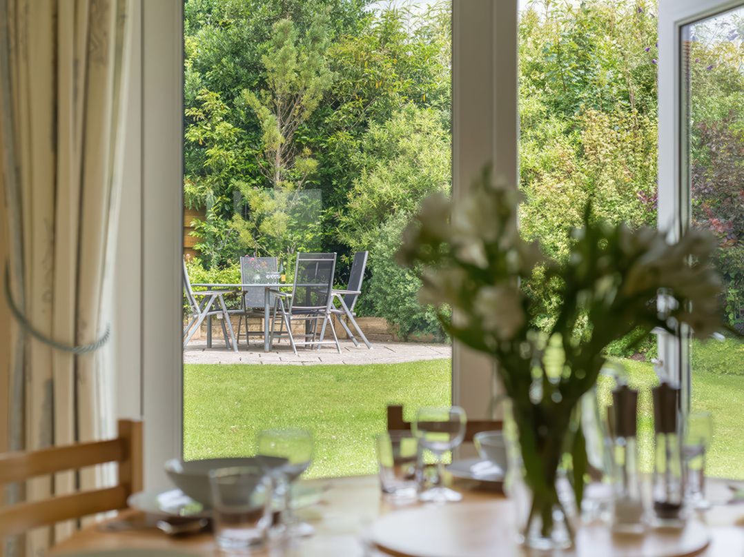 A garden with a patio table and chairs seen through glass doors from a dining table with flowers and glassware at Curlew in Rock