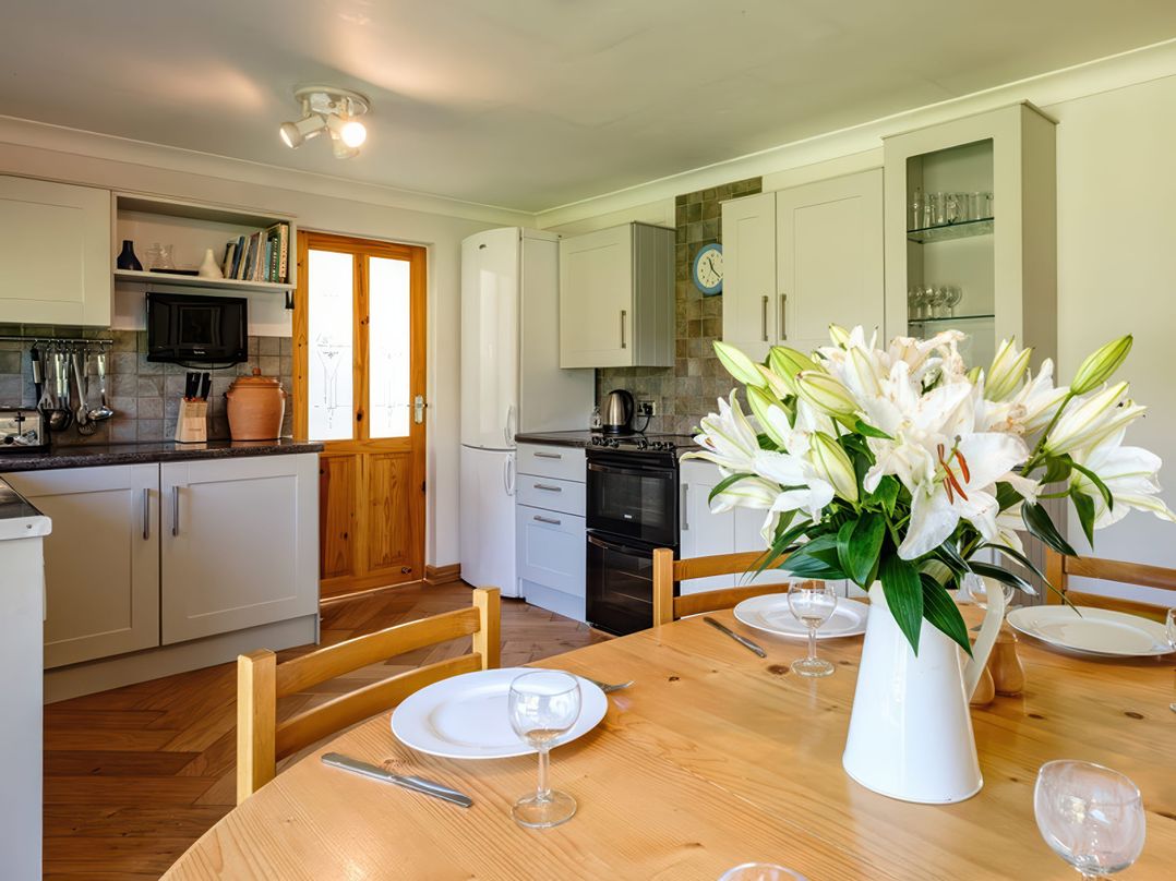 A kitchen with white cabinets a wooden door and a dining table with white flowers at Curlew in Rock