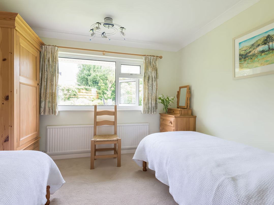 A bedroom with two single beds a wooden chair a wooden wardrobe and a wooden dresser with a mirror and flowers at Curlew in Rock
