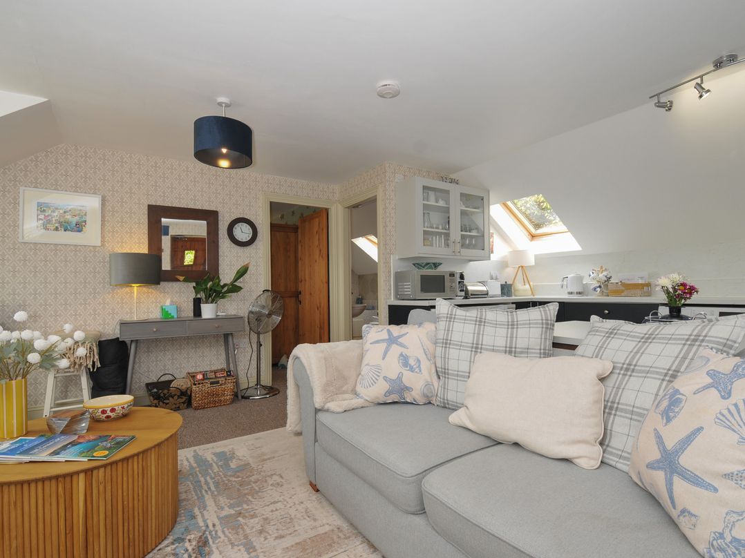 A living room with a sofa, coffee table, and kitchen area at The Hayloft in Lostwithiel