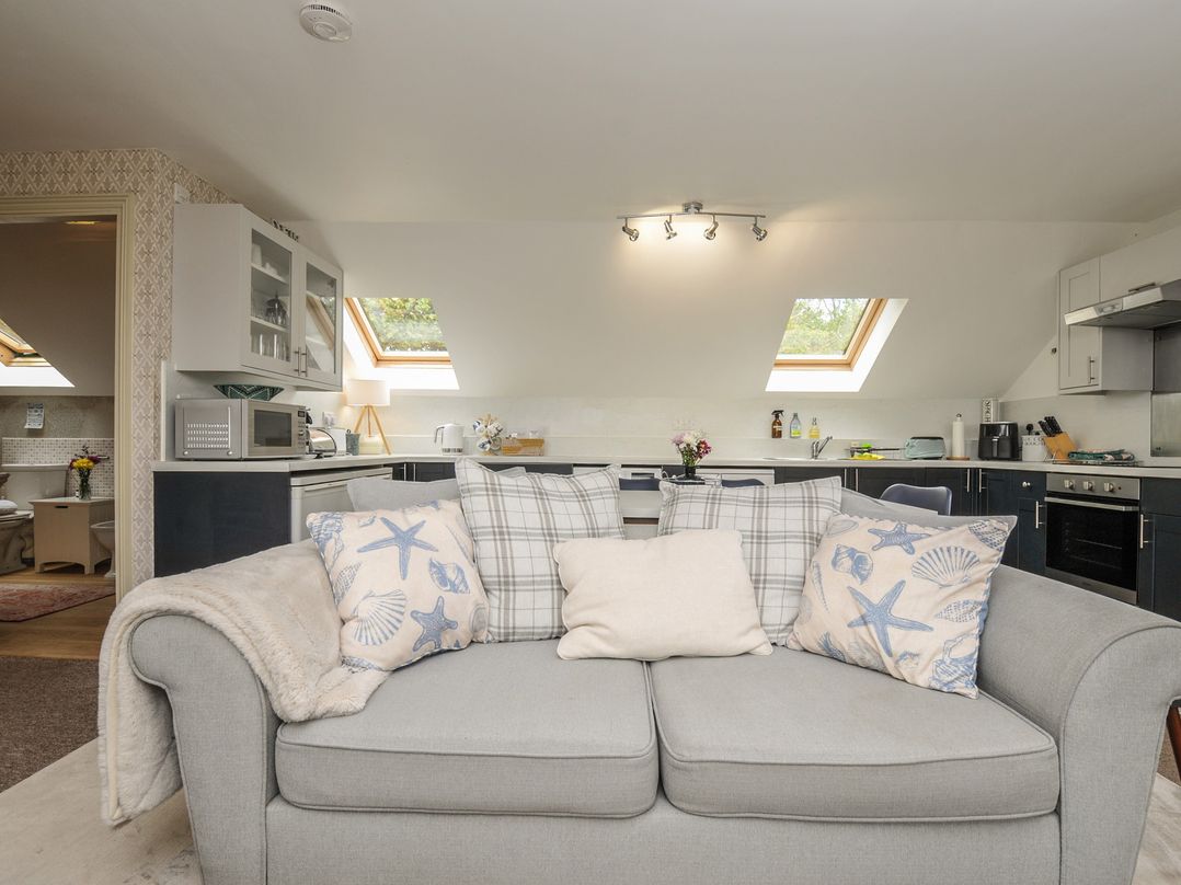 A living room with a sofa and kitchenette features at The Hayloft in Lostwithiel