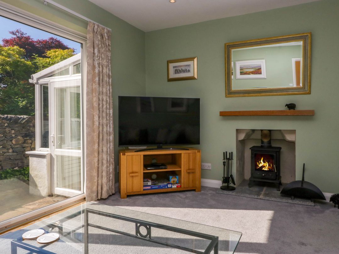 A living room with a flat screen TV on a wooden stand a lit fireplace tools beside it and a glass coffee table at Beckside in Ambleside