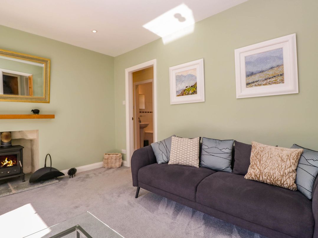 A living room with a dark sofa with cushions a wood burning stove and framed pictures on the wall at Beckside in Ambleside
