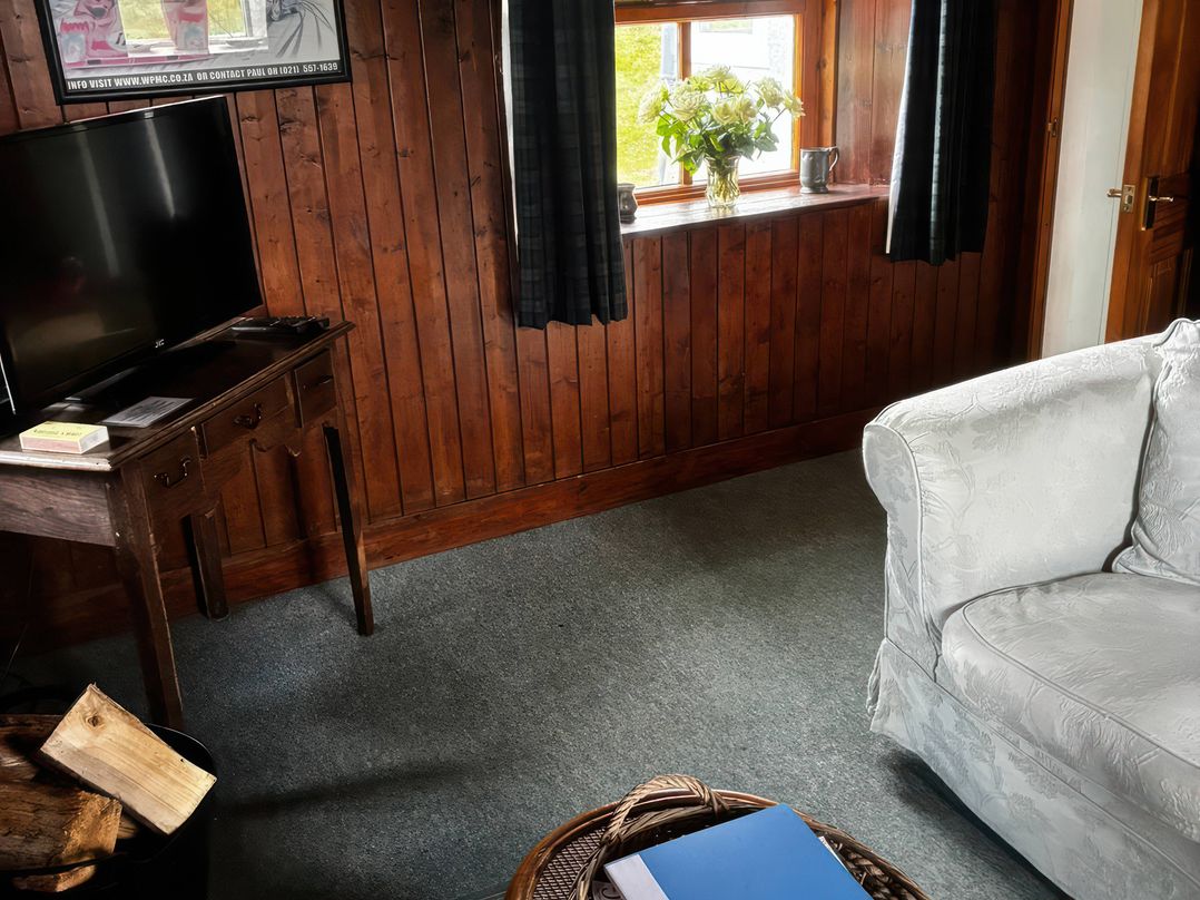 A living room with a tv, table, sofa, and flowers at Strathnoon in Clune near Carrbridge