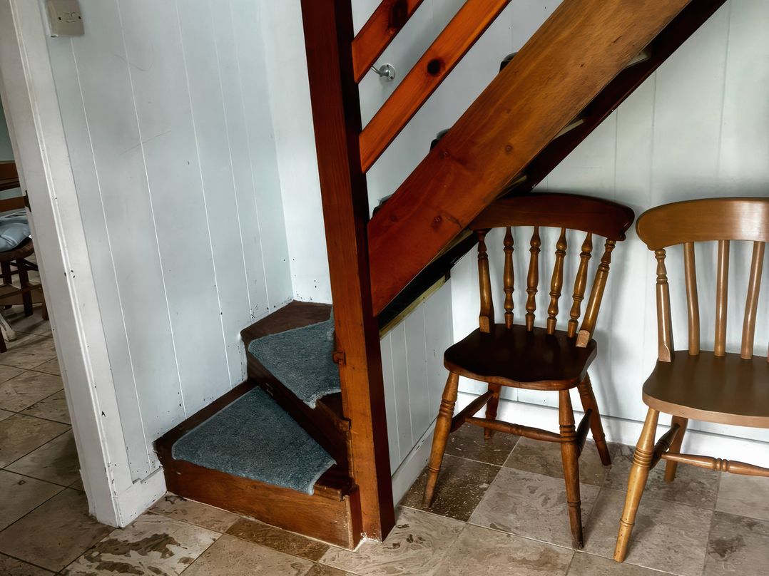 A staircase and two wooden chairs in a hallway at Strathnoon in Clune near Carrbridge