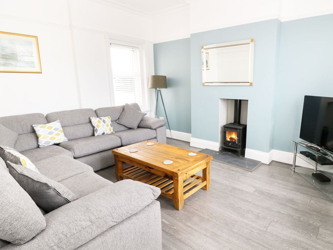 A living room with a grey sectional sofa wooden coffee table a burning stove and a television at 51 Trinity Avenue in Llandudno