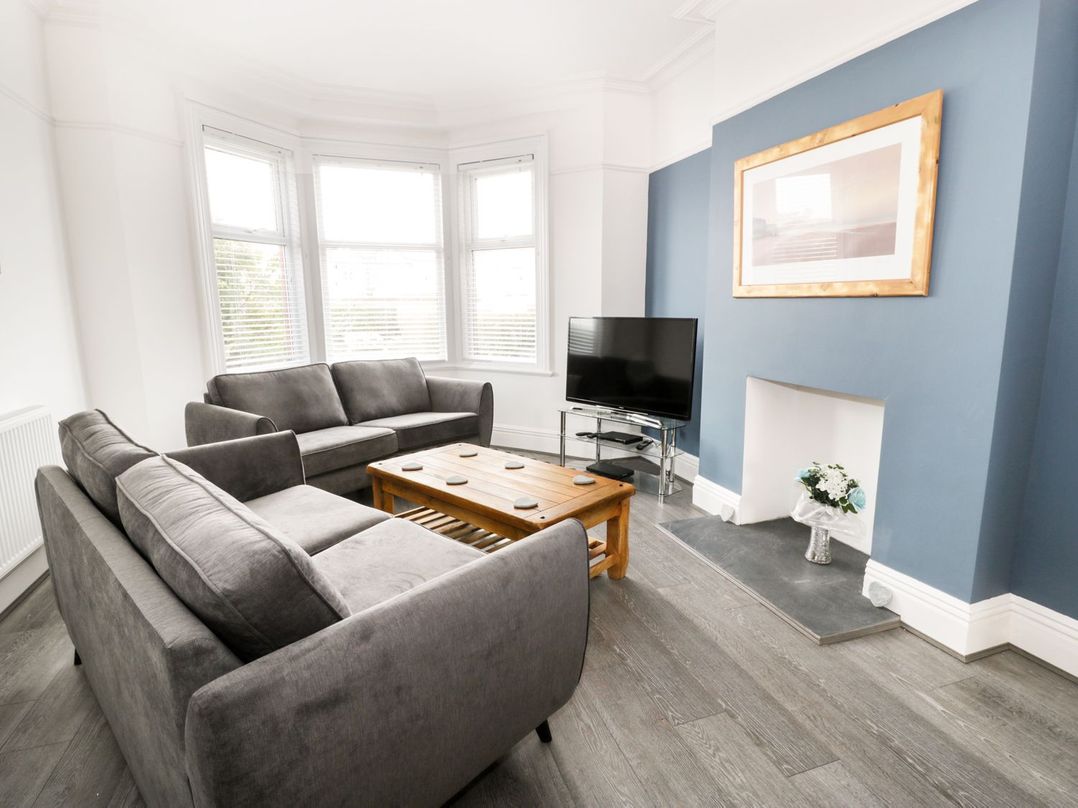 A living room with gray sofas a wooden coffee table a TV on a stand and a blue accent wall at 51 Trinity Avenue in Llandudno