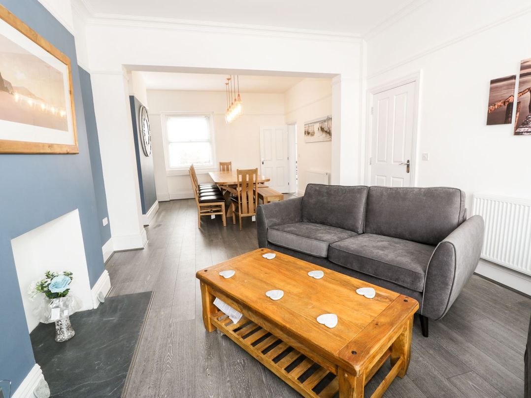 A living room with a gray sofa a wooden coffee table and a dining area with wooden chairs and a table at 51 Trinity Avenue in Llandudno