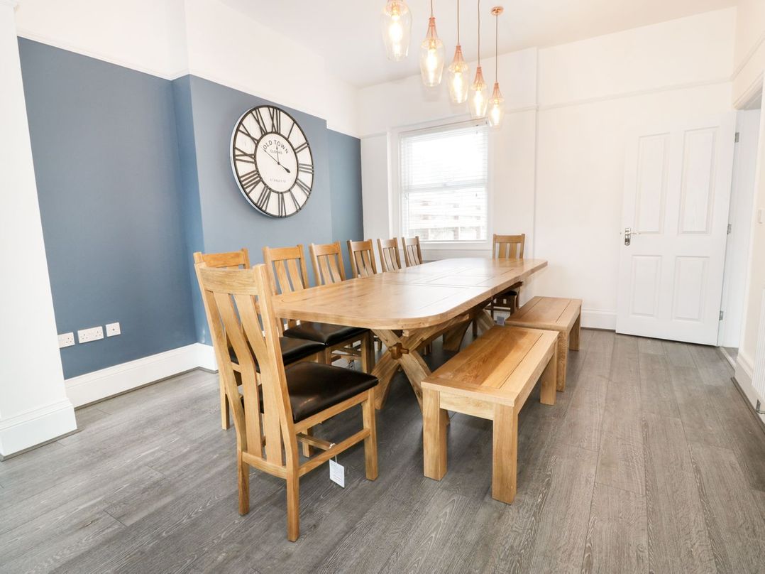 A dining room with wooden table chairs benches and a large wall clock at 51 Trinity Avenue in Llandudno