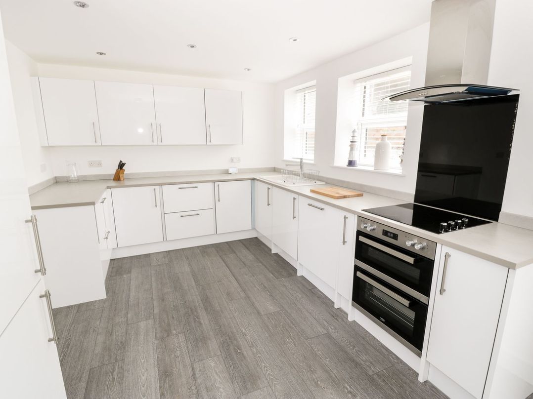 A kitchen with white cabinets a stove and a wooden cutting board at 51 Trinity Avenue in Llandudno