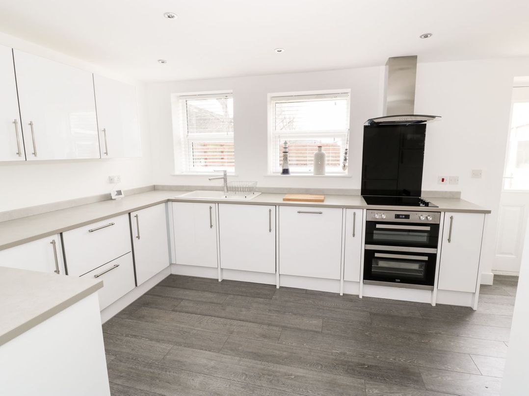A kitchen with white cabinets gray countertops two windows sink stove and oven at 51 Trinity Avenue in Llandudno