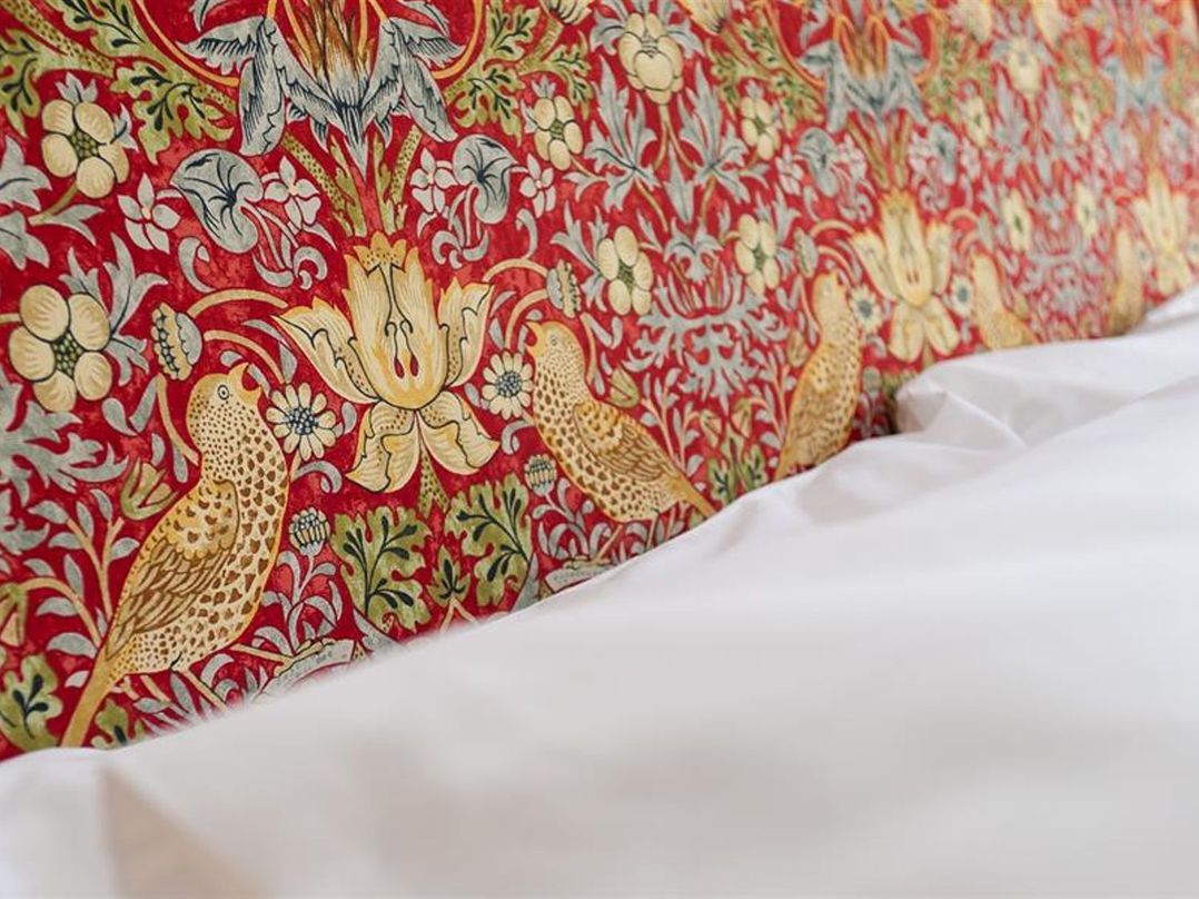 A close up of a fabric headboard with a floral and bird pattern and part of a white bed sheet at Bellflower Cottage in Windermere
