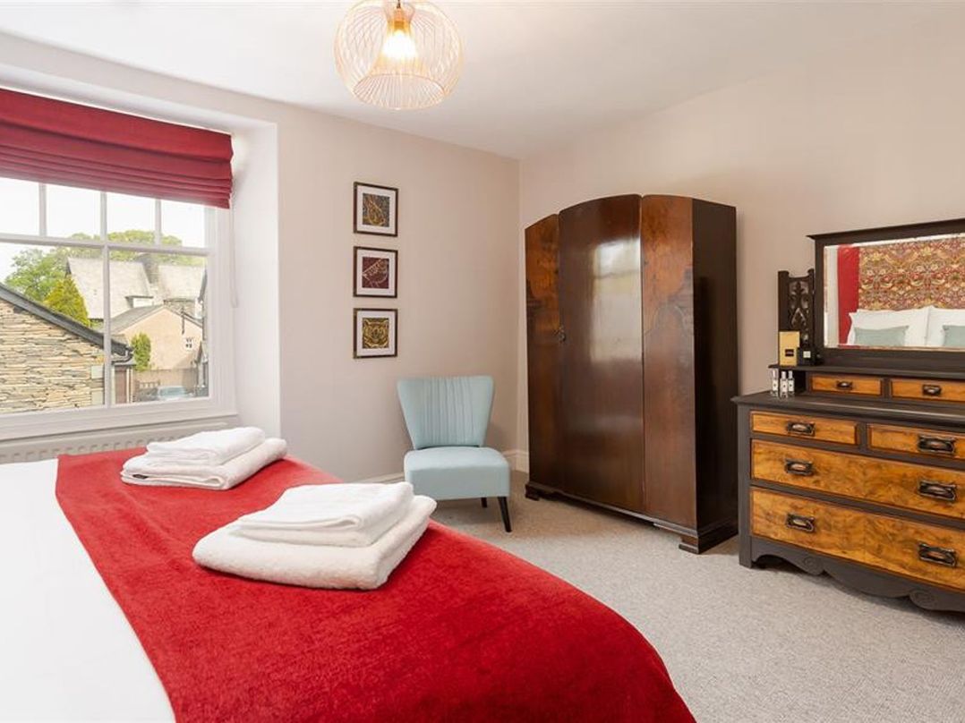 A bedroom with a bed with folded towels and red blanket a blue chair wooden wardrobe and dresser with mirror at Bellflower Cottage in Windermere