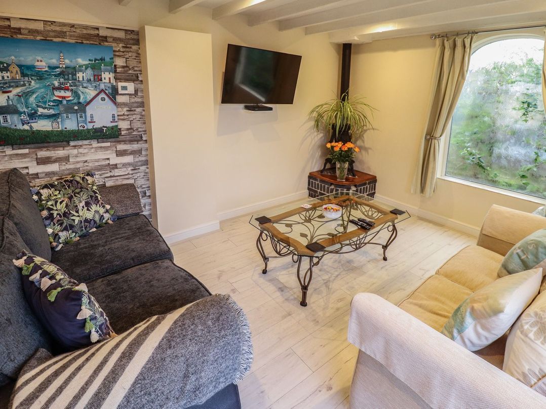 A living room with two sofas a glass coffee table a wall-mounted TV a plant on a corner stand and a large window at Sunnyside in Goxhill near Barrow-Upon-Humber