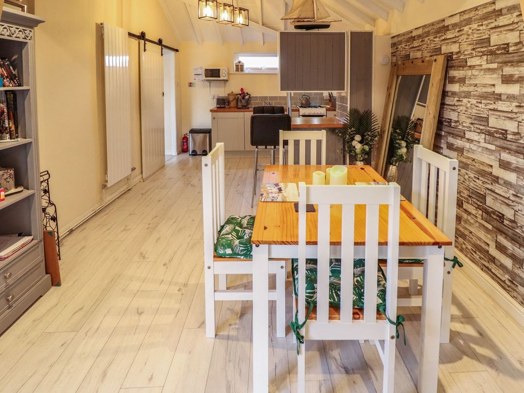 A dining area with a wooden table and white chairs next to a kitchen with stools and cabinets at Sunnyside in Goxhill near Barrow-Upon-Humber