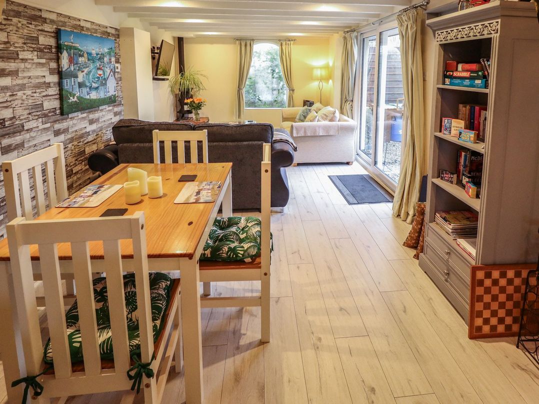 A dining area with a wooden table and white chairs next to a living room with sofas and a bookshelf at Sunnyside in Goxhill near Barrow-Upon-Humber