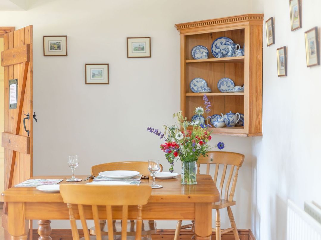 A dining area with a wooden table and chairs flowers in a vase on the table blue and white china on a wooden shelf on the wall at Swallow's Nest in Strefford near Craven Arms