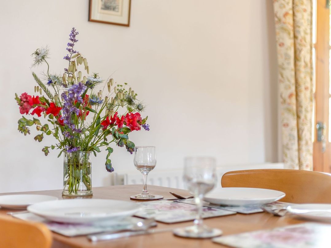 A dining table with plates glasses and a vase of flowers in a room at Swallow's Nest in Strefford near Craven Arms