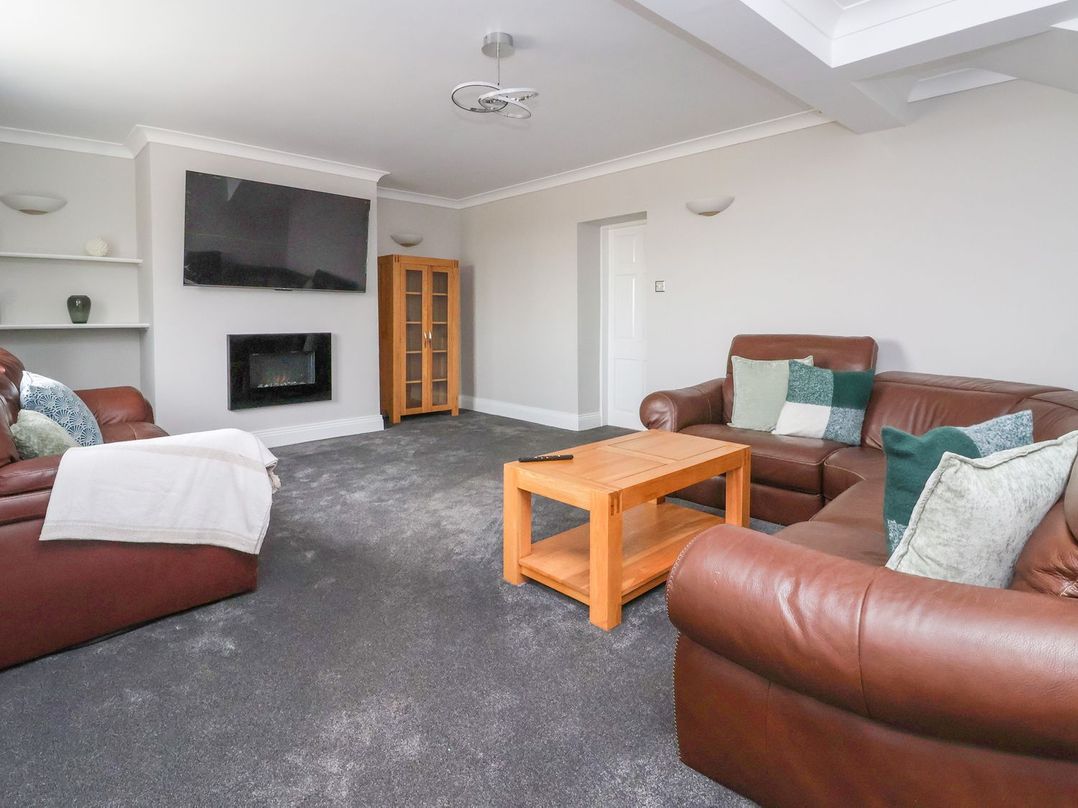 A living room with brown leather sofas a wooden coffee table a wall-mounted television and a fireplace at Bewholme in Skipsea