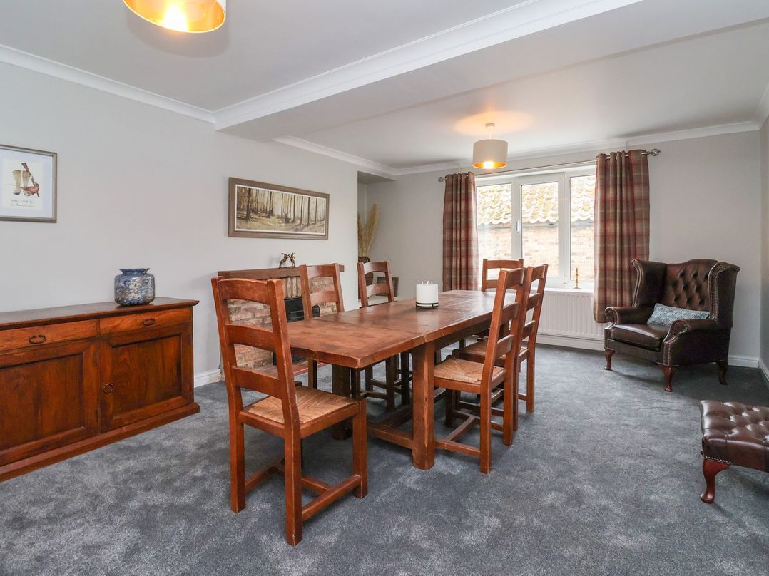 A dining room with a wooden table and six chairs a wooden sideboard a leather armchair and window with curtains at Bewholme in Skipsea
