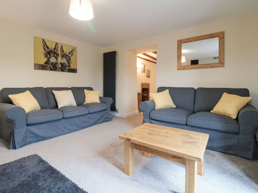 A living room with two gray sofas and yellow pillows a wooden coffee table and a painting of two donkeys at Lane Head Cottage in Alderwasley near Wirksworth