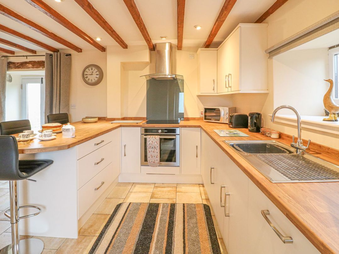 A kitchen with wooden countertops a sink oven stovetop bar stools and a striped rug at Lane Head Cottage in Alderwasley near Wirksworth